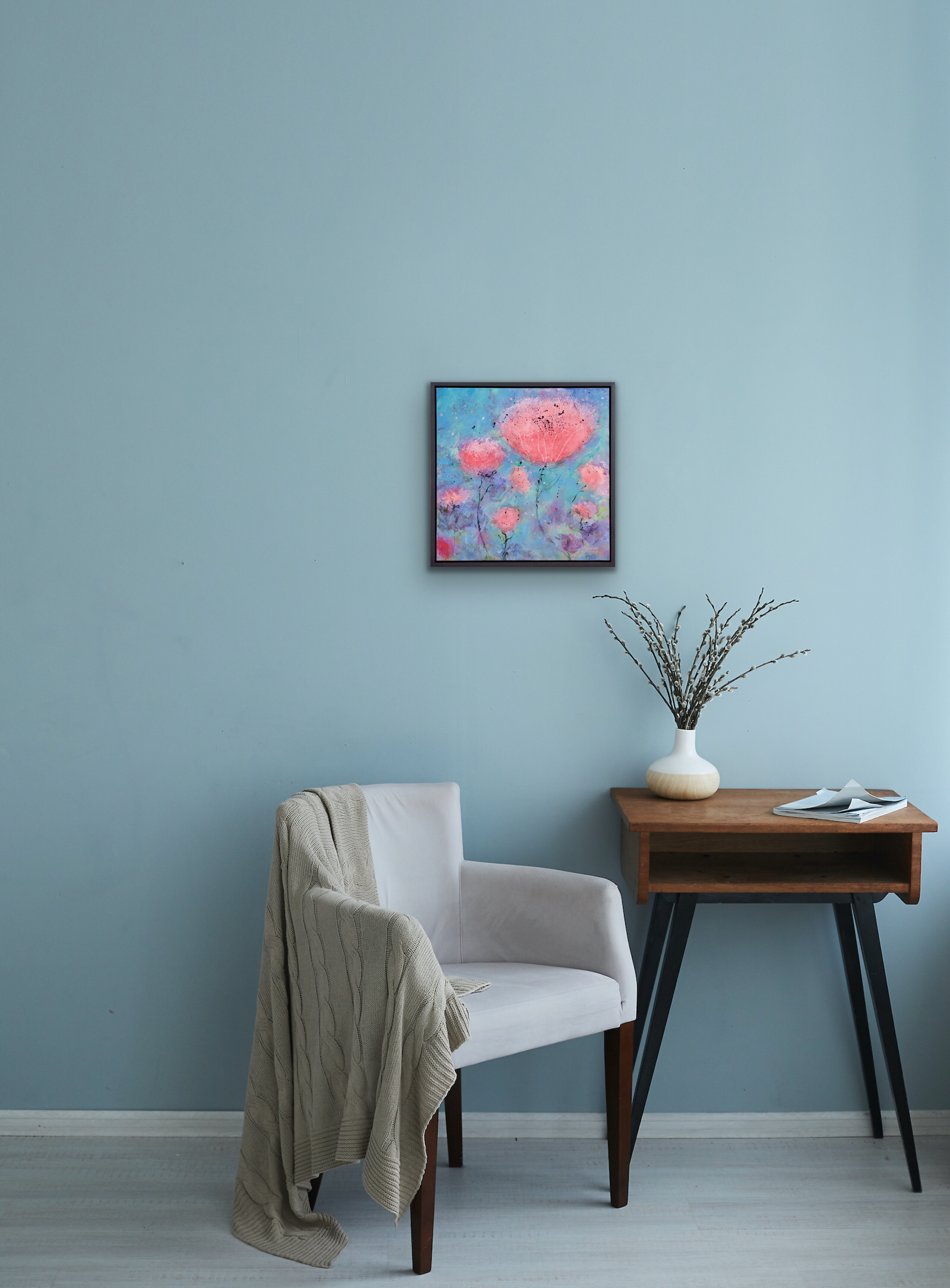 Painting shown by a reading chair and side table on a blue wall