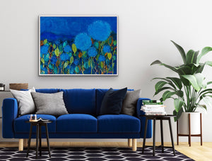 Predominantly blue floral painting shown above a blue velvet sofa.