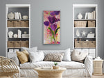 Load image into Gallery viewer, This strong purple, coral, and green floral vertical painting is displayed in a neutral living room setting to inject a pop of colour into the space.
