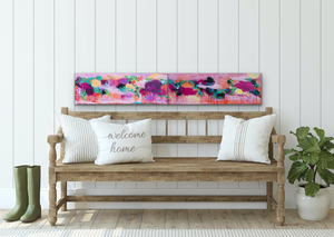 Two paintings (shown as a Diptych) shown above a wooden bench with 3 pillows - 1 says Welcome Home
